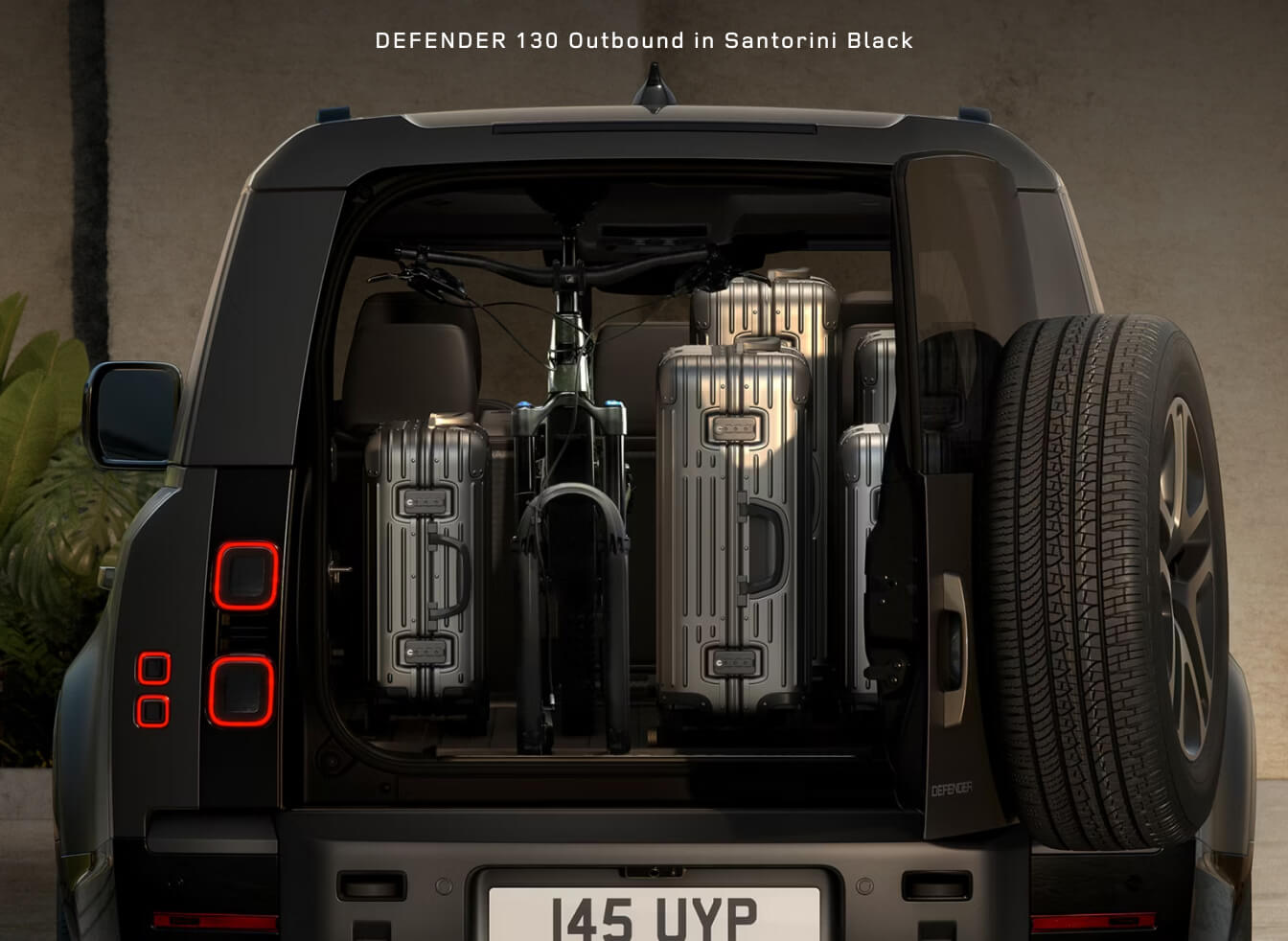Rear trunk view of a Land Rover Defender 130 Outbound in Santorini Black packed with silver suitcases and a bicycle.
