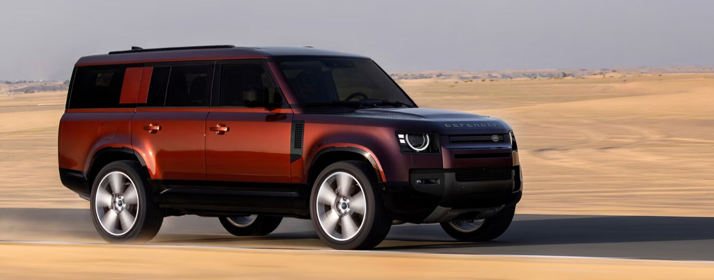 2026%20Land%20Rover%20Defender%20-%20sand.png Red 2026 Land Rover Defender driving on a desert road