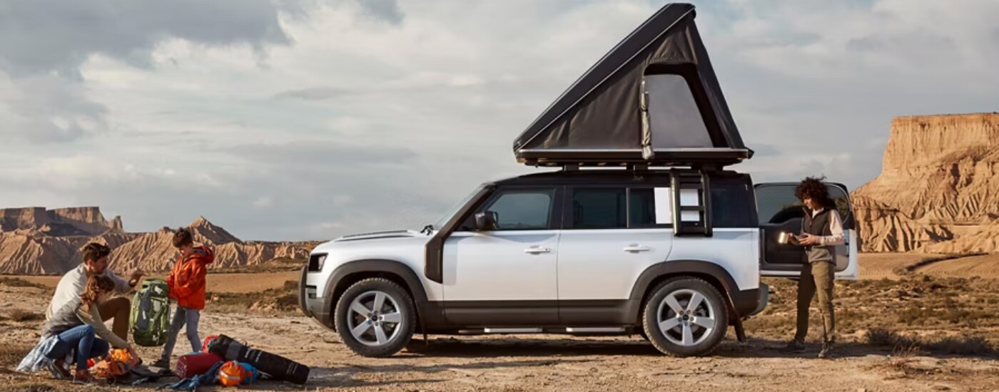 2026%20Land%20Rover%20Defender%20-%20tent.png Silver 2026 Land Rover Defender 90 with a roof-top tent parked off-road
