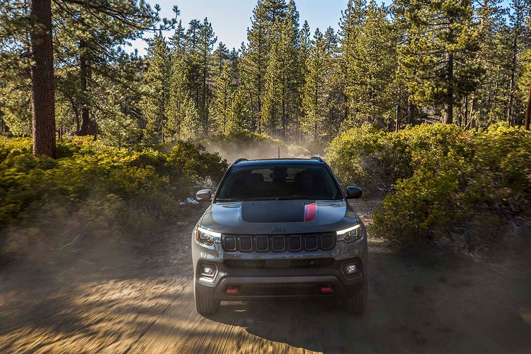 Vue avant du Jeep Compass Trailhawk 2022 roulant sur une piste de terre battue en forêt