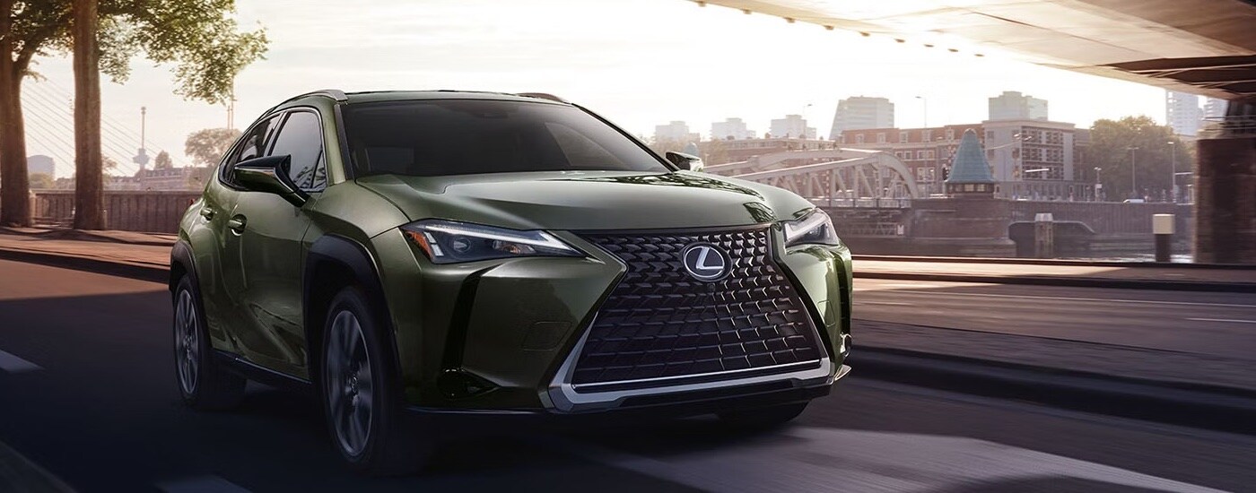 A green 2025 Lexus UX Hybrid driving on a city highway.