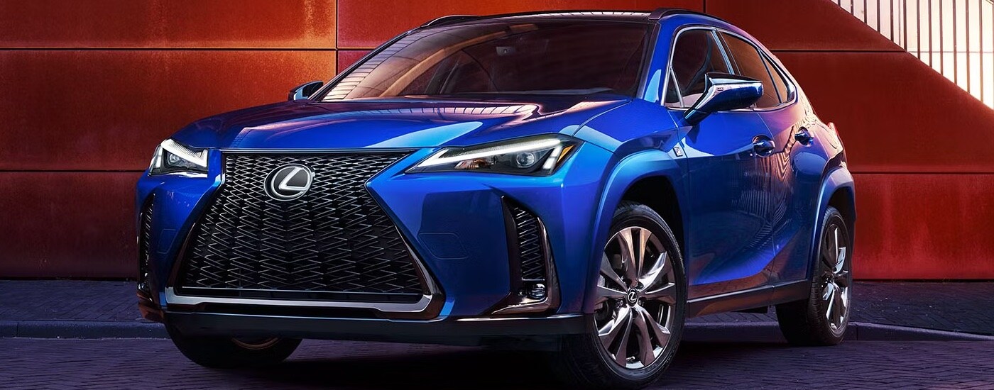A blue 2025 Lexus UX Hybrid parked in front of a red wall.
