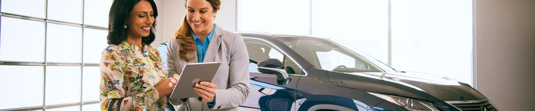A saleswoman helping a female customer look over paperwork in front of a New Lexus