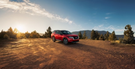 Nissan Pathfinder red Nissan Pathfinder parked outside with trees and mountains in the background