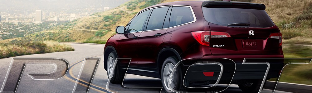 The New Honda Pilot driving towards the city Deep Red Honda Pilot driving down a curvy road