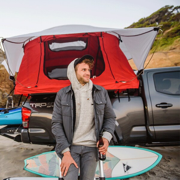 Great Summer Yakima Accessories include cargo racks, kayak/paddleboard racks and tow hitches for boats Young man smiling next to his Toyota Tacoma featuring a Yakima Truck Bed Tent, Yakima Racks with bottle openers, Yakima Kayak straps and Rack and Yakima Surfboard Rack