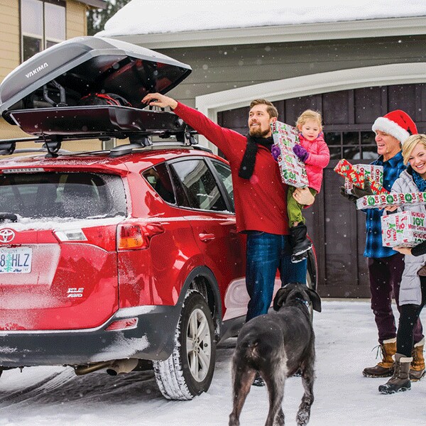 Great Yakima Winter Accessories include ski and snowboard racks and Cargo Compartments Family in sweaters loading Christmas Presents into a Yakima Covered Cargo pod on top of a Toytoa Highlander