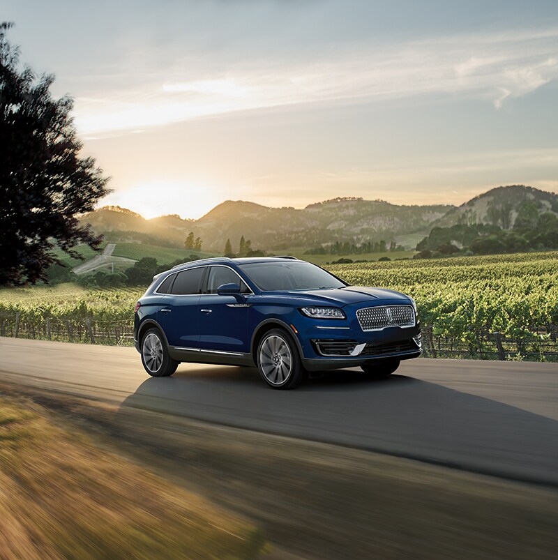 Lincoln of New Bern is a Car Dealership in New Bern near Bridgeton, NC | Dark Blue 2020 Lincoln Nautilus driving on country road with farmland in background