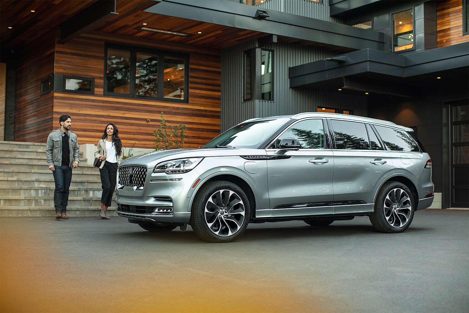 Lincoln of New Bern is a Car Dealership in New Bern near Neuse Forest, NC | Young well dressed couple approaching silver 2020 Lincoln Aviator parked outside building