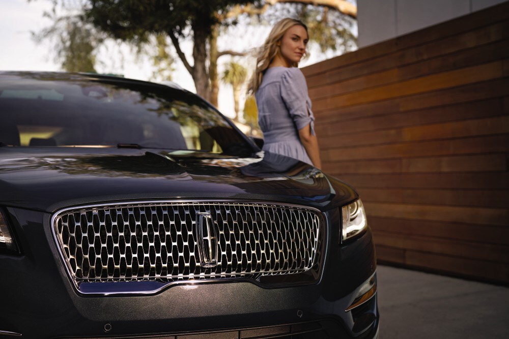 Lincoln of New Bern is a Car Dealership in New Bern near River Bend, NC | Closeup of Black 2020 Lincoln Continental grille with woman standing in background
