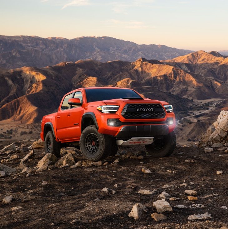 2023-Toyota-Tacoma-TRDPro-CrewMax-Truck.png bright orange Toyota Tacoma TRD truck parked in a rocky area at a steep angle