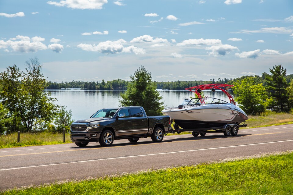 2022-RAM-1500-Limited-CrewCab-Truck-L07.png black Ram 1500 Limited truck towing a boat next to a lake
