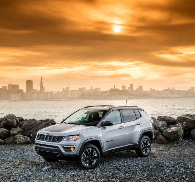 2022-Jeep-Compass-Trailhawk-SUV.png white Jeep Compass SUV parked at a waterfront overlooking the city
