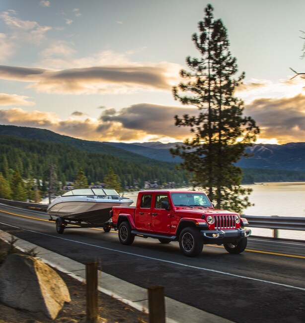 2023-Jeep-Gladiator-Rubicon-Truck-red.png red Jeep Gladiator truck towing a boat on a tree-lined highway