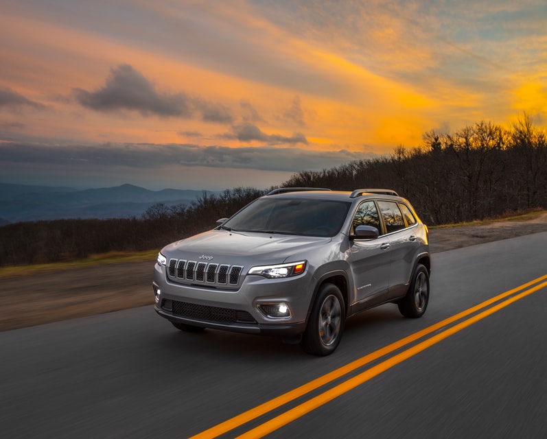 2019-Jeep-Cherokee-Limited-SUV-L01 (1).png silver Jeep Cherokee SUV driving down a highway at sunset