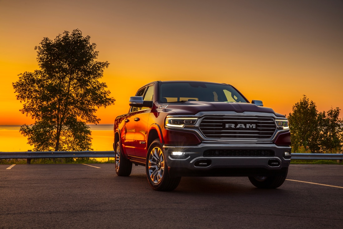 2023-RAM-1500-LaramieLonghorn-ShortBox-CrewCab-Truck-L01.png red Ram 1500 truck parked near a waterfront at sunset