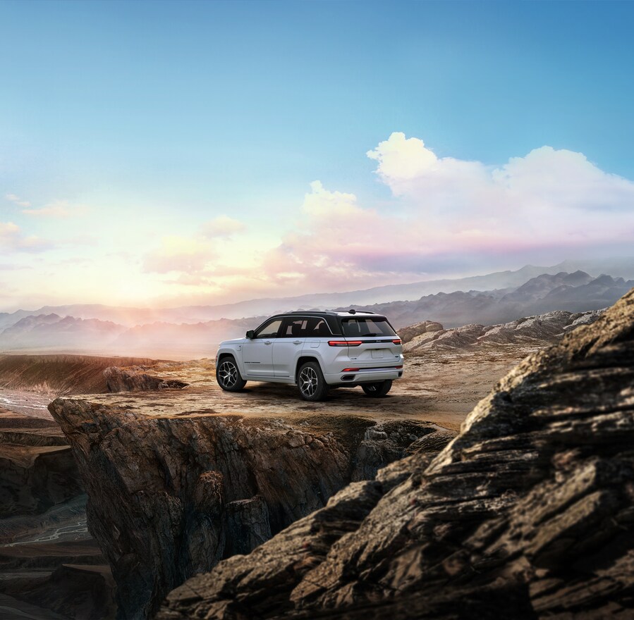 white Jeep Grand Cherokee parked on a ridge with a blue sky in the background