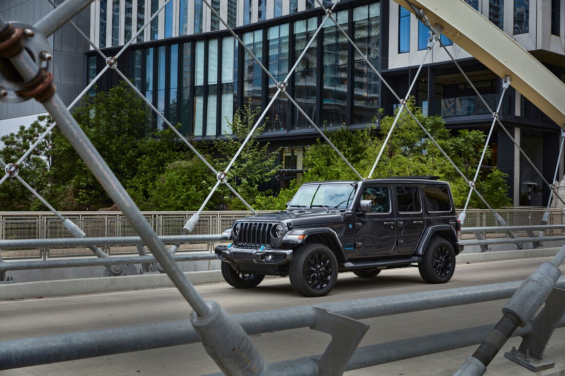 2024-Jeep-Wrangler-Sport4xe-SUV-L02.png grey Jeep Wrangler driving across a city bridge