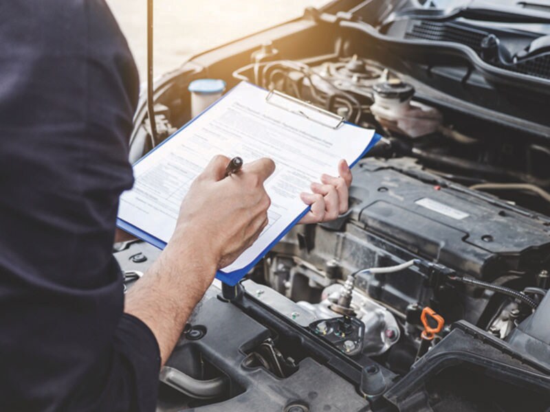 Vehicle Evaluation A person standing over a car engine with a clipboard taking notes.