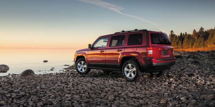 2014-Jeep-Patriot-Latitude.png red Jeep Patriot SUV parked on a pebble beach