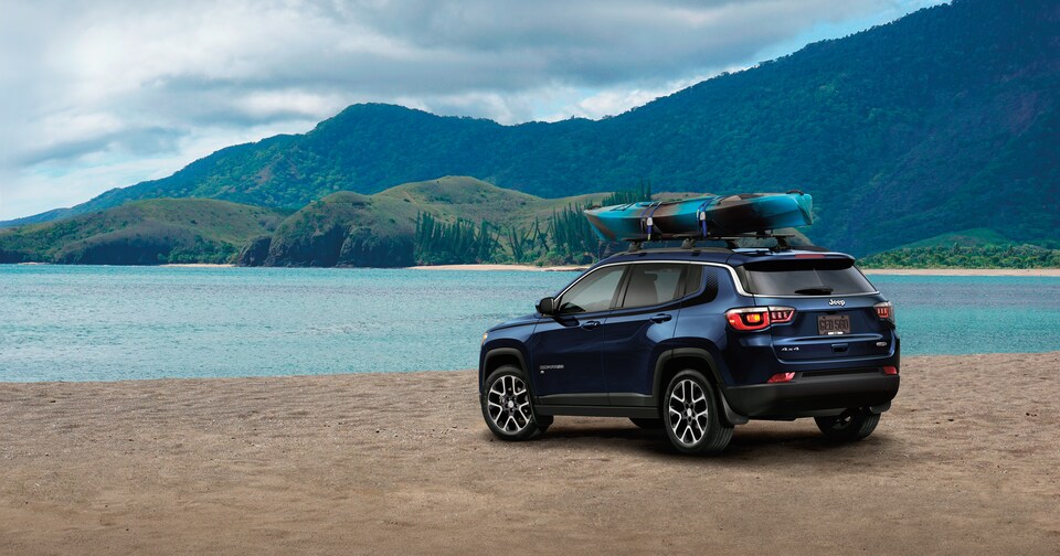 2021-Jeep-Compass-Latitude-SUV-L05.png deep blue Jeep Compass parked on a beach with a kayak on the roof-rack