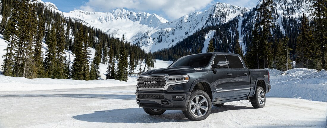 2024-RAM-1500-Limited-CrewCab-Trucks.png black Ram 1500 truck parked in the snow next to evergreens and mountains