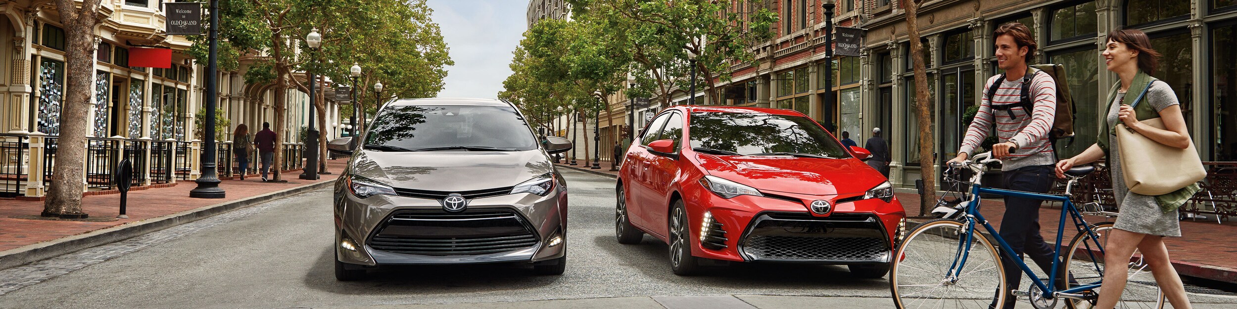 red and tan Toyota cars at a stop sign with people walking by with a bike