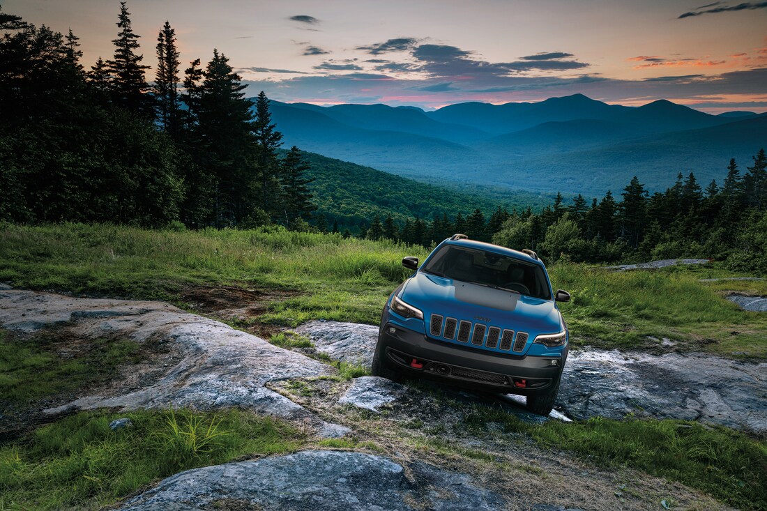 2023-Jeep-Cherokee-Trailhawk-SUV-L10.png blue Jeep Cherokee parked at an angle in a mountain field