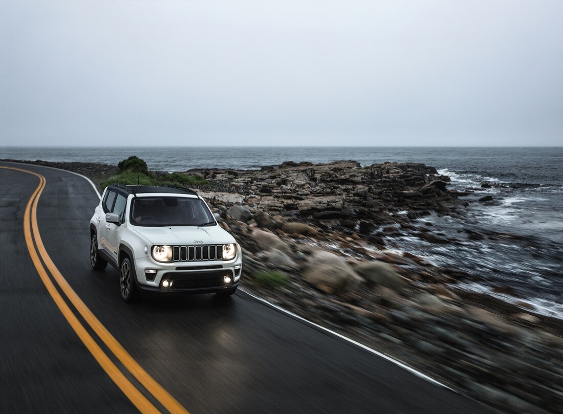 2023-Jeep-Renegade-Limited-WheelAddOn-SUV-L02.png white Jeep Renegade driving near a stormy, rocky shoreline