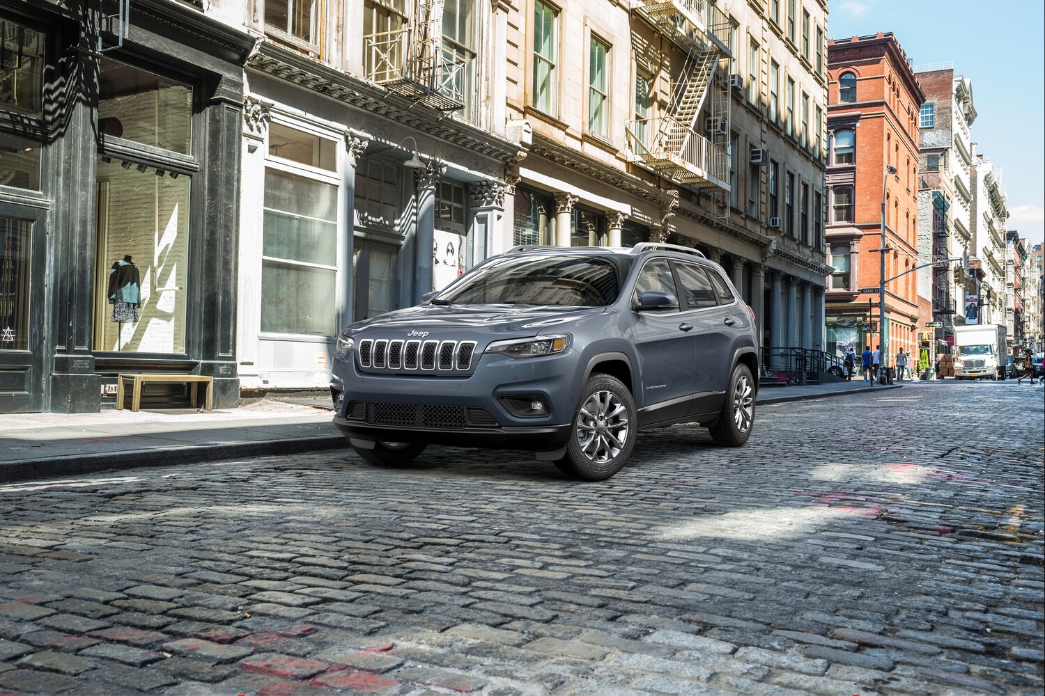 2022-Jeep-Cherokee-LatitudeLux-SUV-L01.png gray Jeep Cherokee SUV parked on cobblestone streets, next to a city building