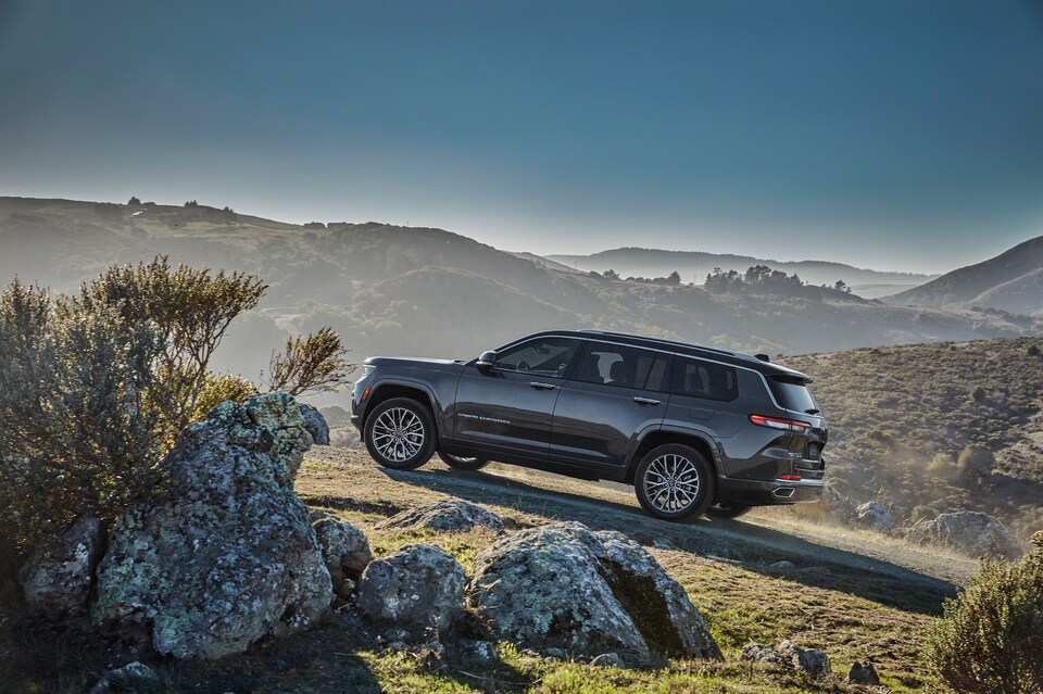 2021-Jeep-GrandCherokeeL-SummitReserve-SUV-L04.jpeg dark gray Jeep Grand Cherokee L SUV driving up a rocky hill