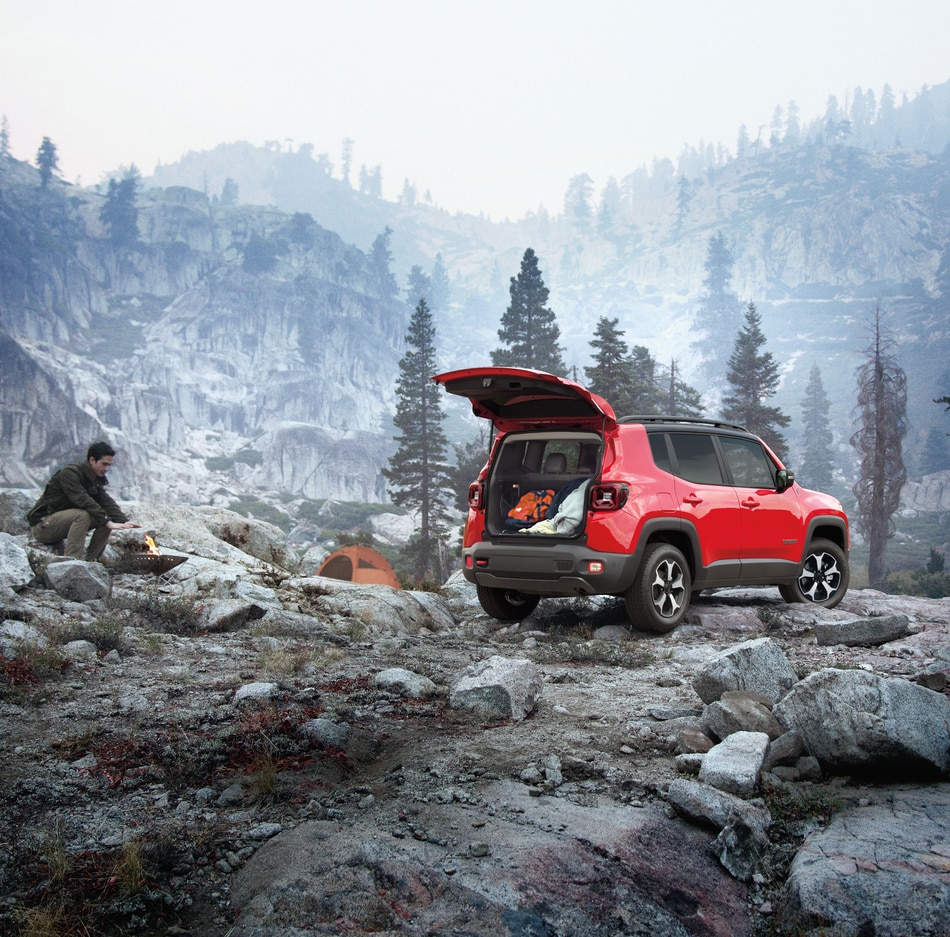 2021-Jeep-Renegade-Trailhawk-SUV.png red Jeep Renegade SUV parked on a rocky outcropping with the trunk open and a camper nearby