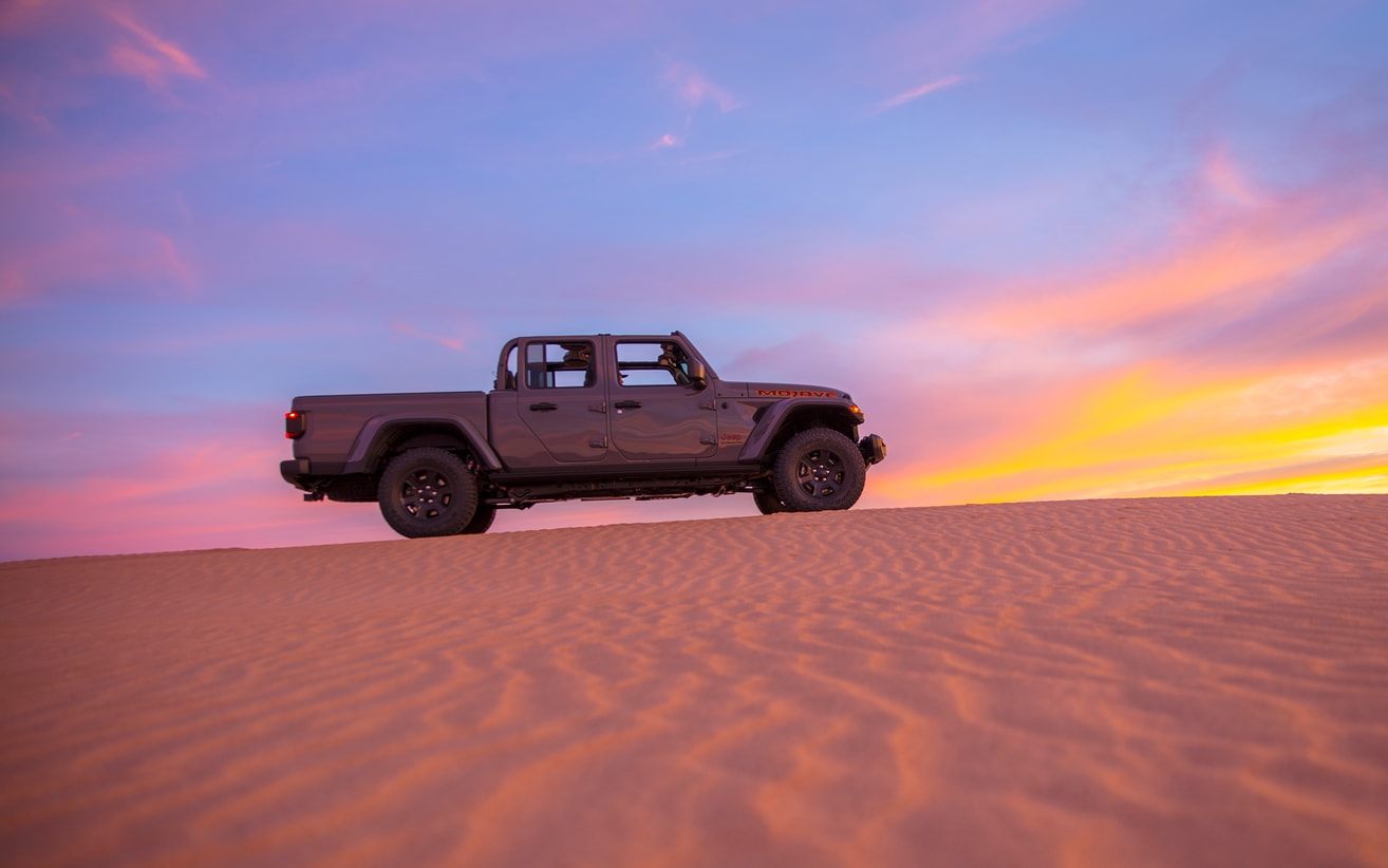 2021-Jeep-Gladiator-Mojave-Truck-L08.png Jeep Gladiator truck driving at the top of a sand dune at sunset