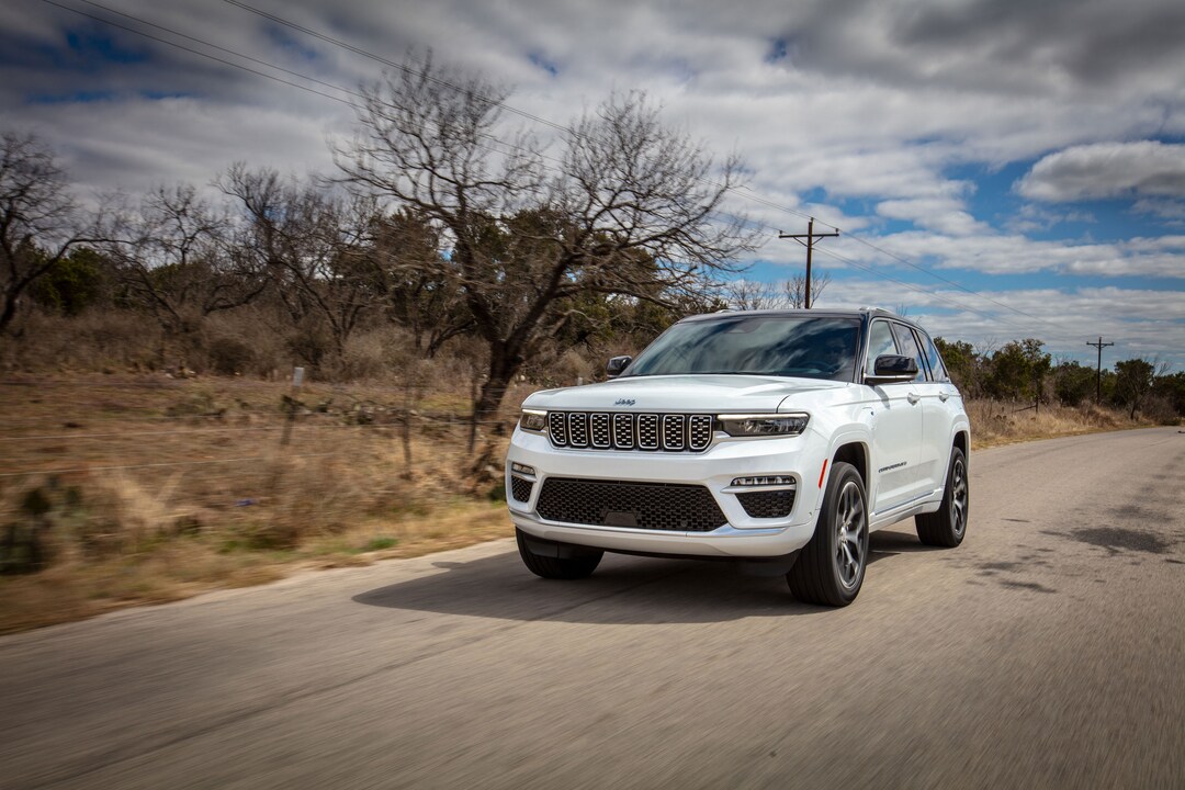 Jeep white Jeep Grand Cherokee driving on a road with dead trees along with side