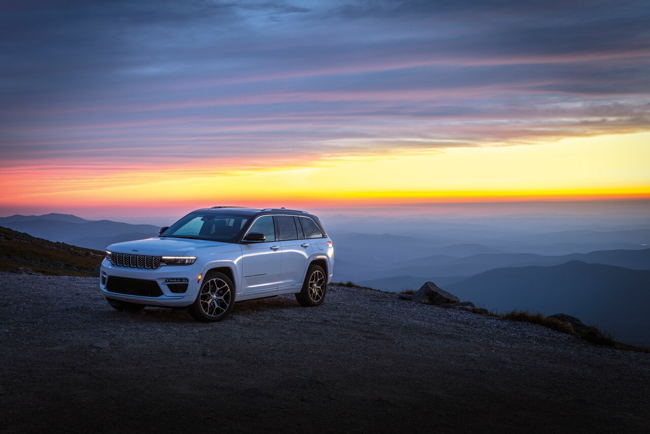 Jeep white Jeep Grand Cherokee 4xe parked on a ledge overlooking a cloudy valley at sunrise