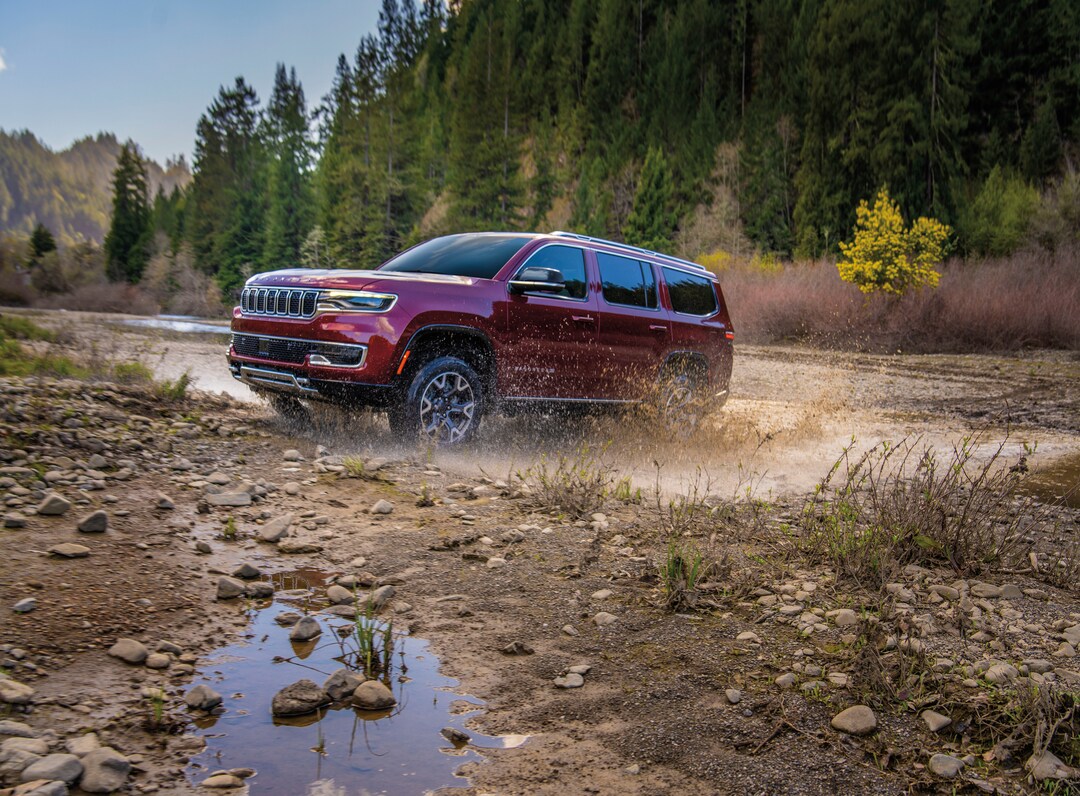 Jeep dark red Jeep Wagoneer driving through a muddy river bed