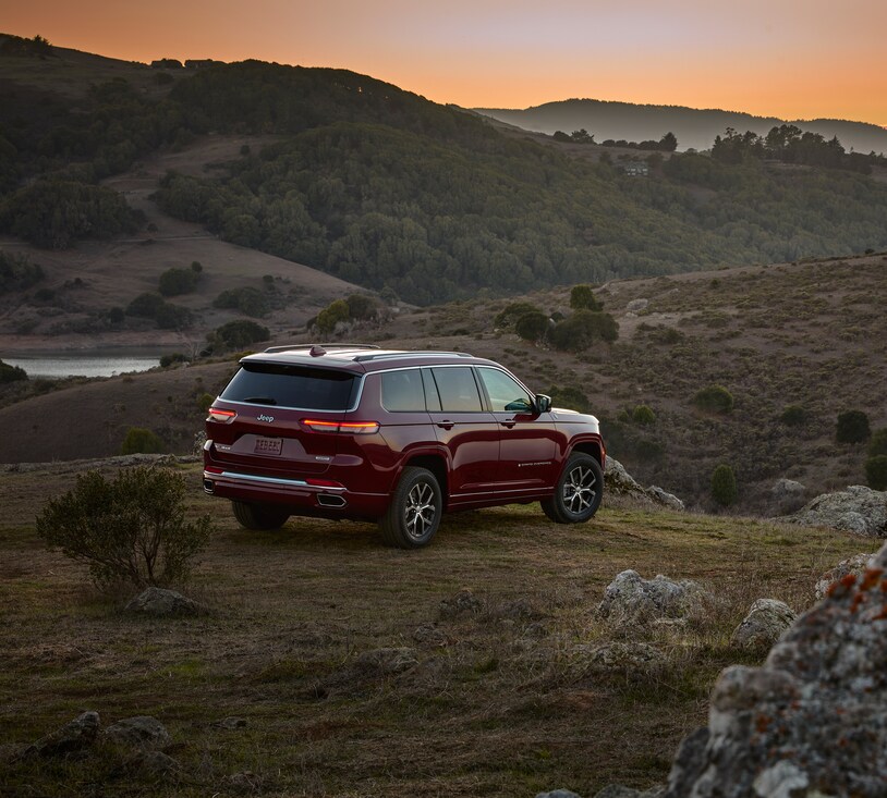 2021-Jeep-GrandCherokeeL-Limited-SUV.png maroon Jeep Grand Cherokee L third-row SUV parked on a ledge overlooking a hill covered in sagebrush