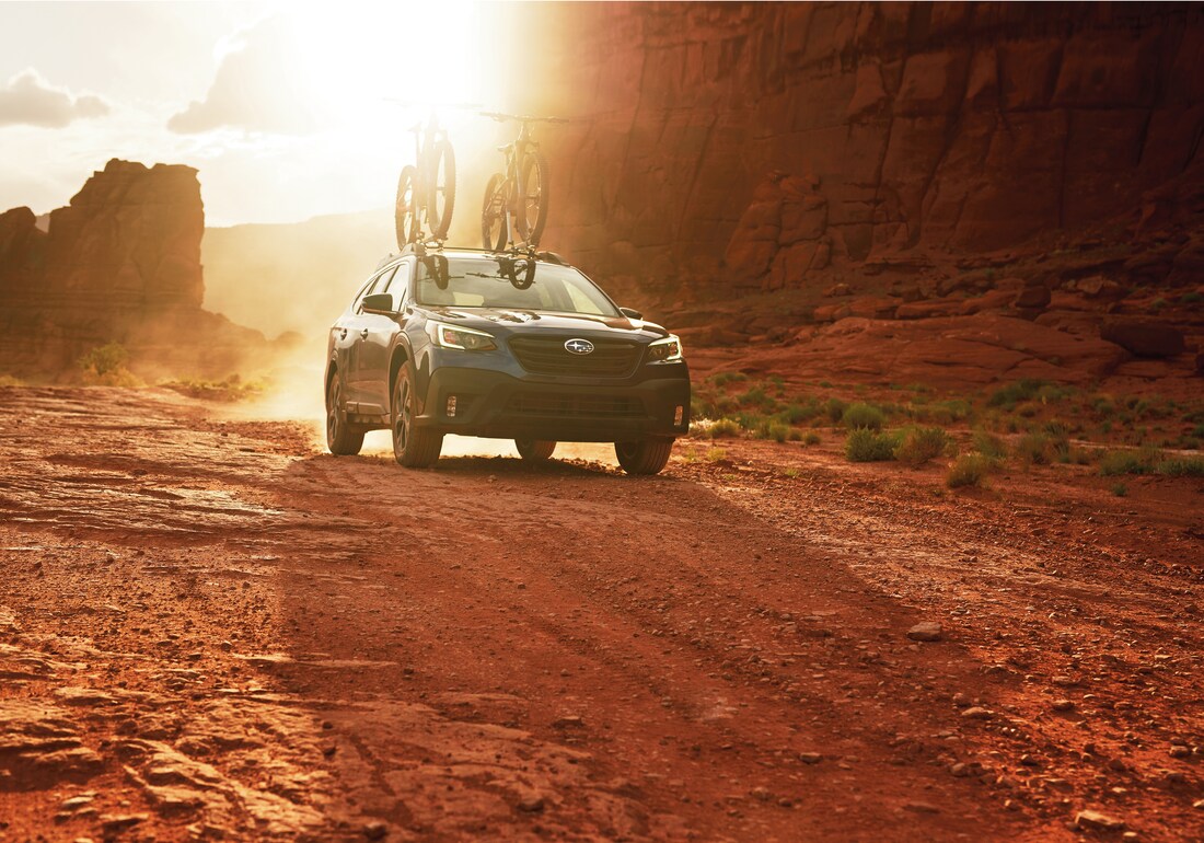 2022-Subaru-Outback-OnyxEditionXT-SUV-L11.png blue Subaru Outback SUV driving through the desert with bikes on a roof rack