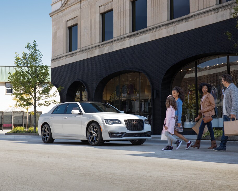 2022-Chrysler-300-S-RedPackage-Sedan.png Chrysler 300 S sport sedan parked in front of a storefront with a family walking by