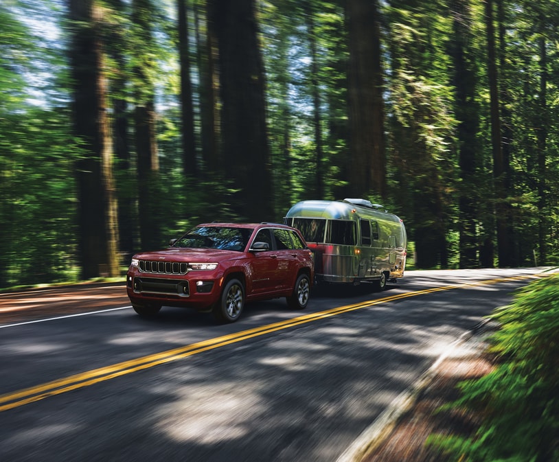 maroon Jeep Grand Cherokee towing an Airstream trailer in the woods