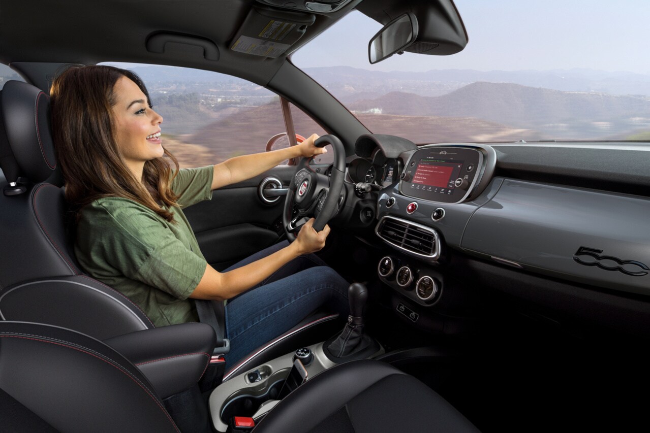 female driver in a green shirt at the wheel of a FIAT with a black and grey interior