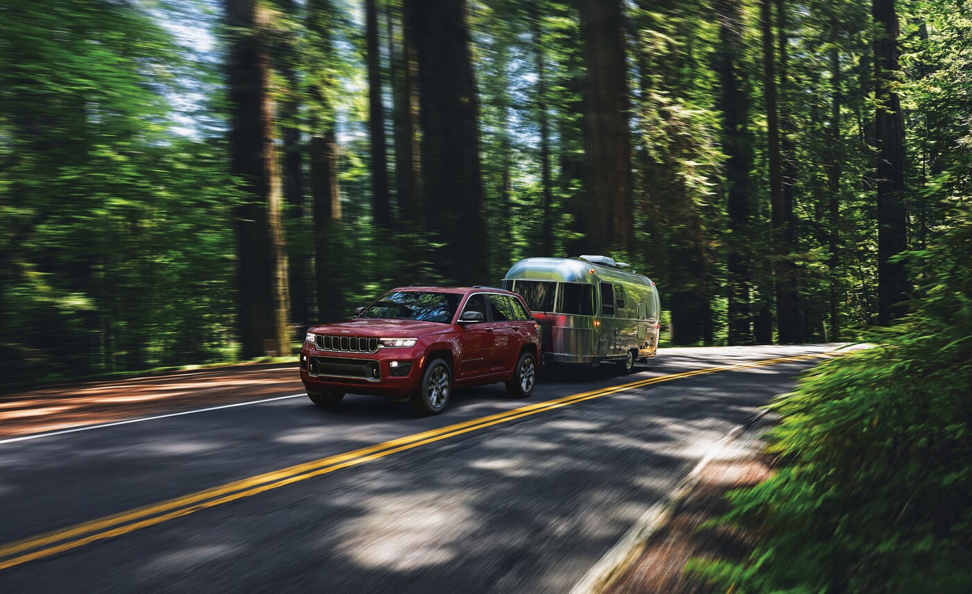 red Jeep Cherokee towing an airstream on a forest road