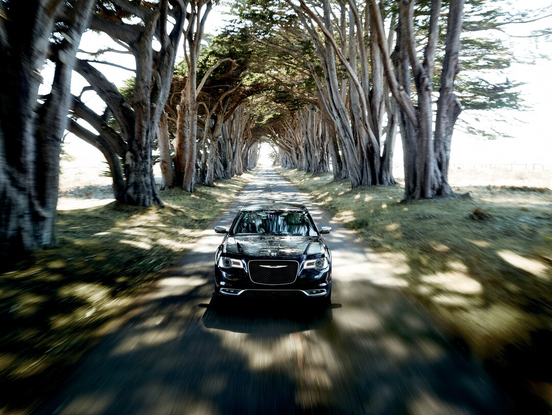 Chrysler 300 black Chrysler 300 sedan driving on a tree lined road
