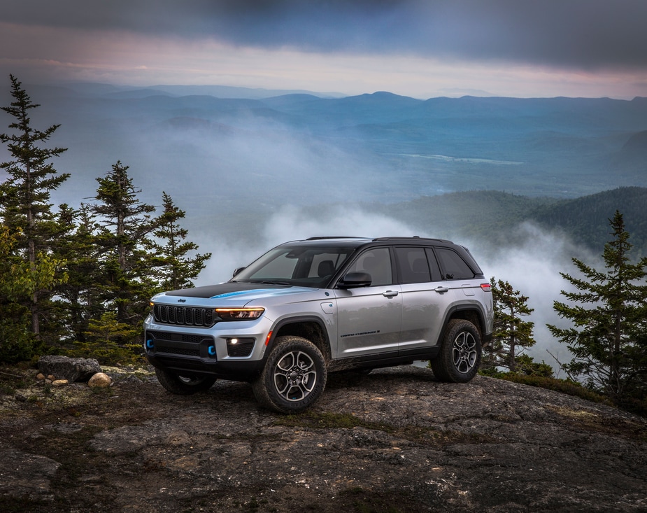 2023-Jeep-GrandCherokee-Trailhawk-4xe-SUV-L15.png silver Jeep Grand Cherokee 4xe SUV parked atop a large rock overlooking a cloudy valley