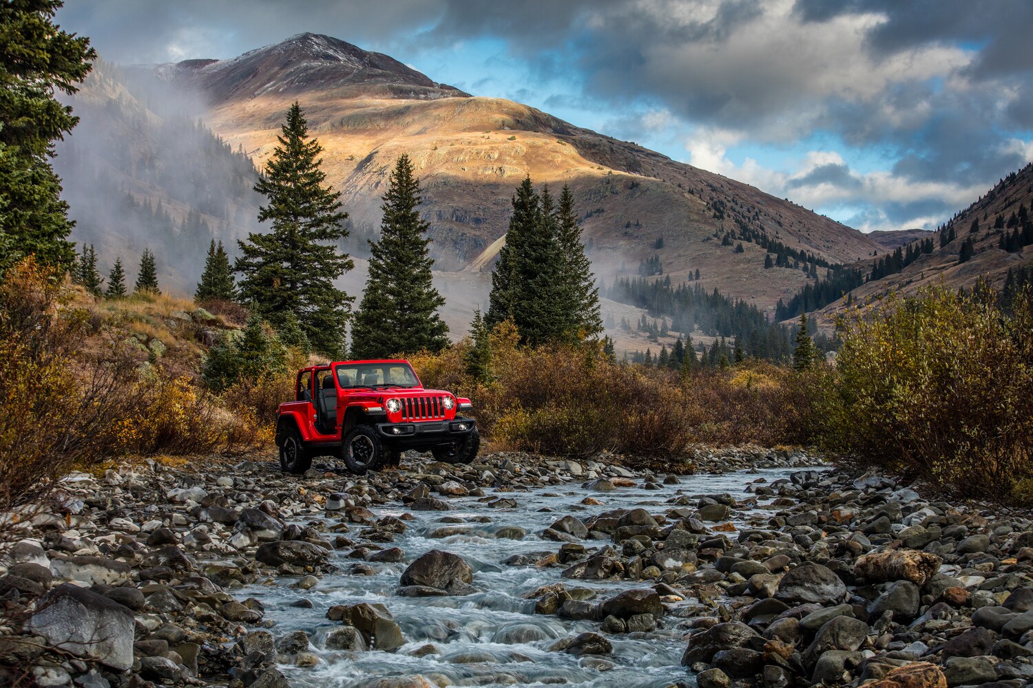 2021-Jeep-WranglerJL-Rubicon-2Door-SUV-L12.png red Jeep Wrangler JL Rubicon SUV bouldering over river rocks, mountains in the background
