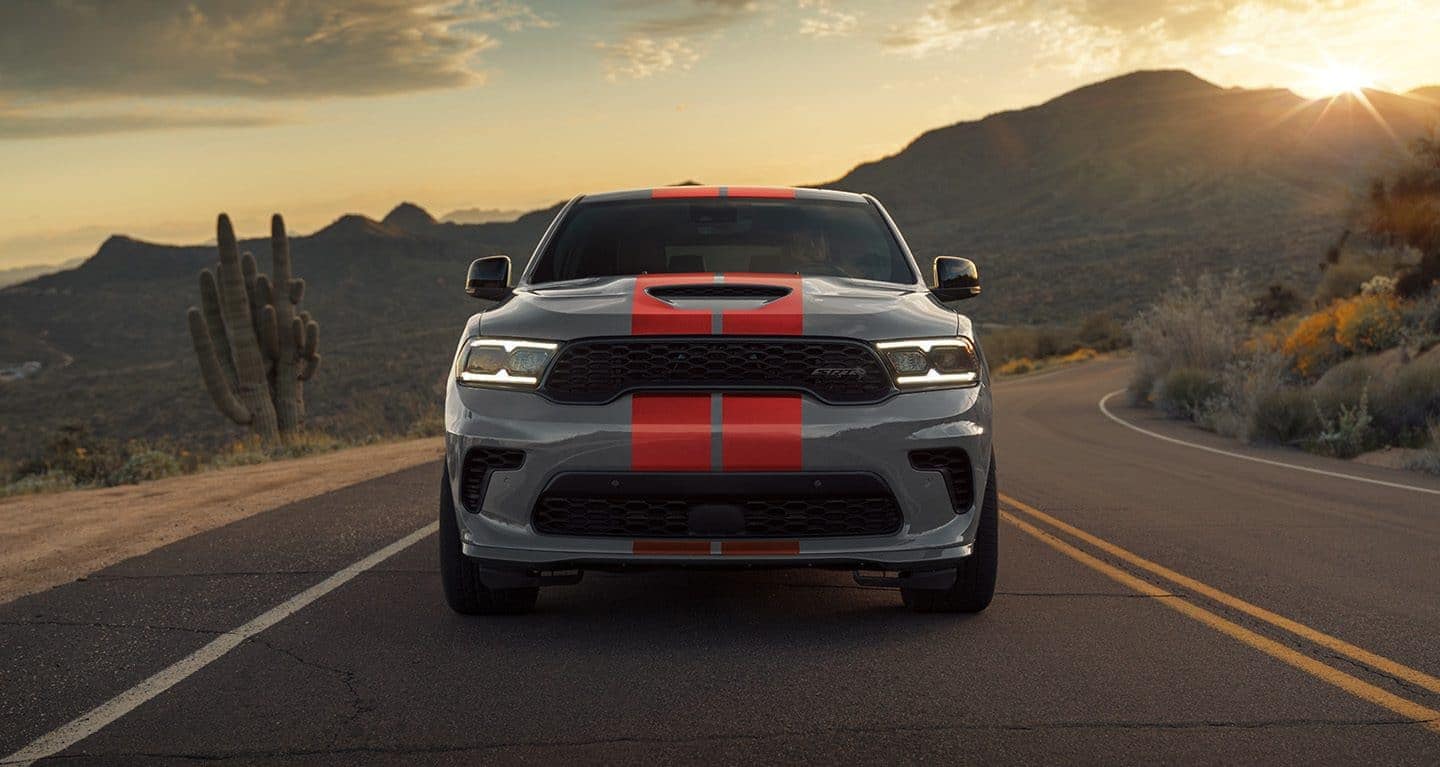 silver Dodge Durango SUV with a red stripe down the middle driving on a road at sunset