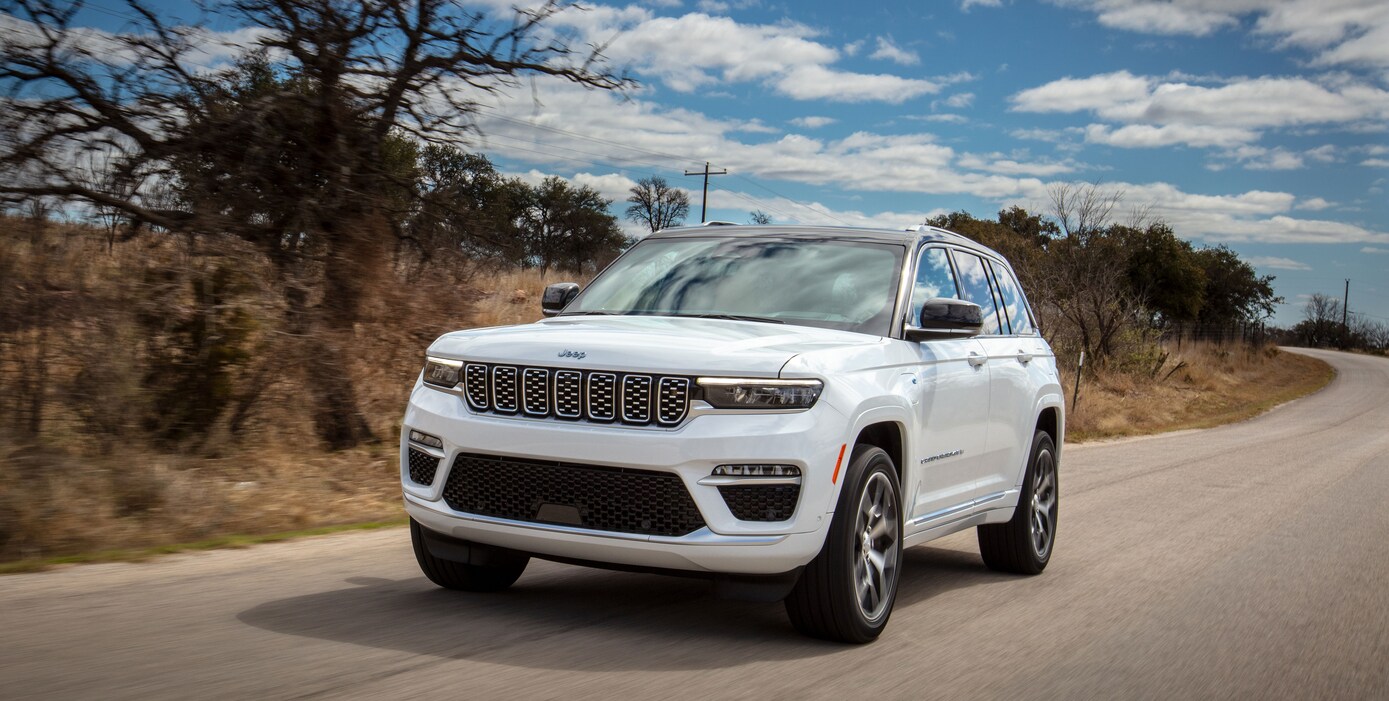 white Jeep Grand Cherokee driving on a road lined with sage brush