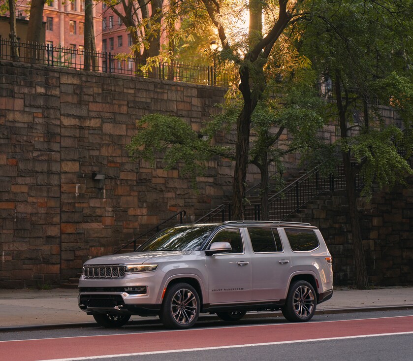 2023-Jeep-GrandWagoneer-SeriesIII-SUV.png silver Jeep Grand Wagoneer SUV parked in front of a large stone wall