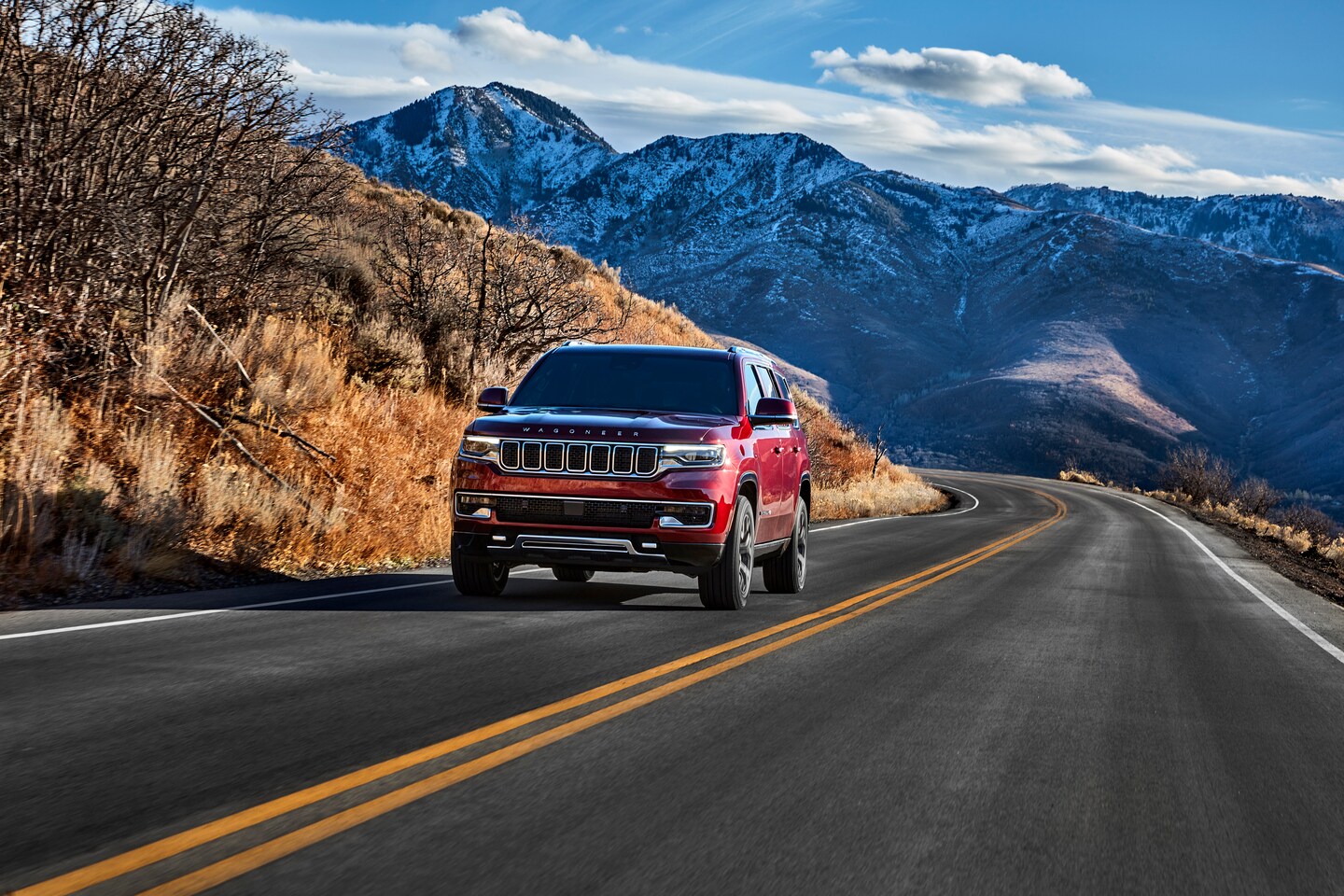 red Wagoneer driving on a road with mountains in the background