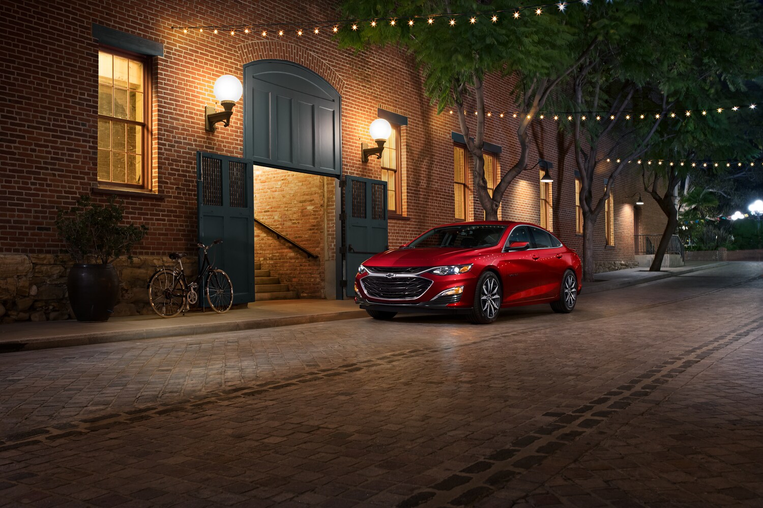 2021-Chevrolet-Malibu-RS-Sedan-L01.png red Chevy Malibu sedan parked outside of a low-lit brick building